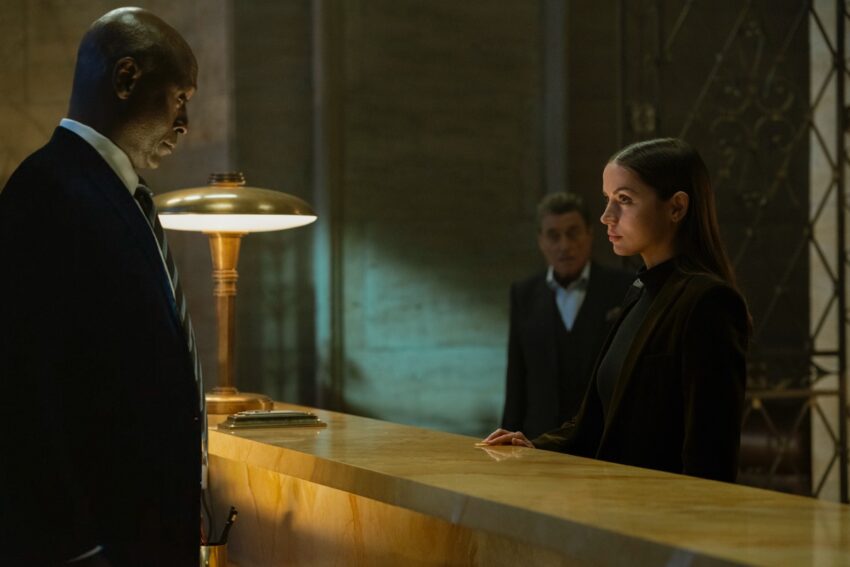 elegant black man man behind a hotel reception desk greeting a young woman checking in.